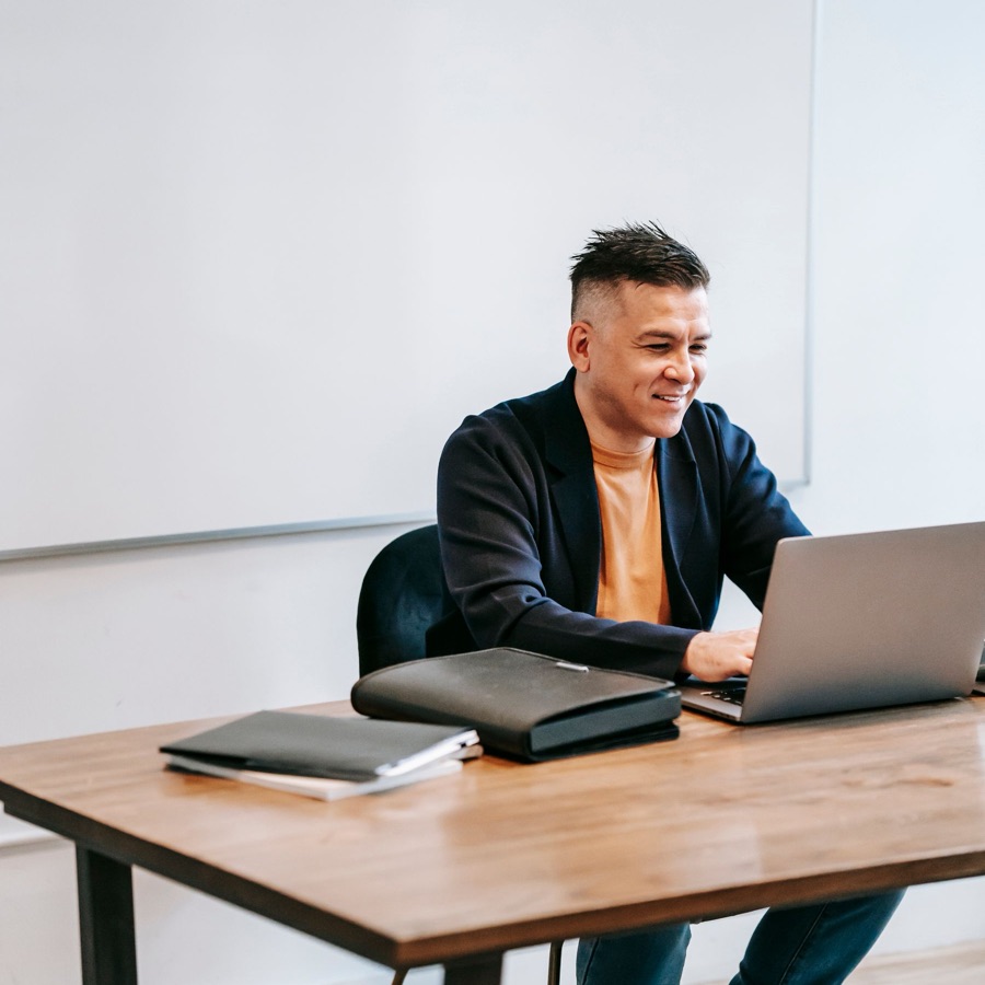 Un hombre sonriente, en su oficina y frente al computador, con su trabajo al día