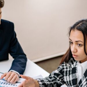 Un hombre y una mujer revisan gráficos y documentos ante un computador para ordenar los gastos y las compras de tecnología